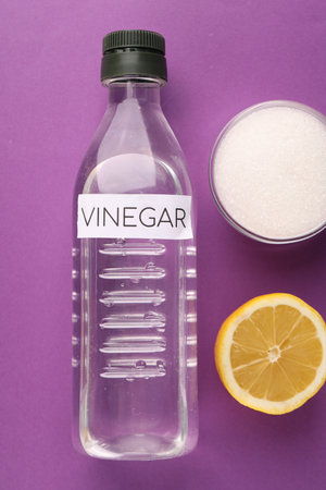 Eco friendly natural cleaners. Vinegar in bottle, cut lemon and bowl of soda on purple background,...