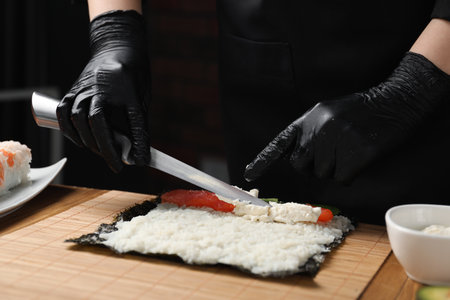 Chef in gloves making sushi roll at wooden table, closeupの写真素材