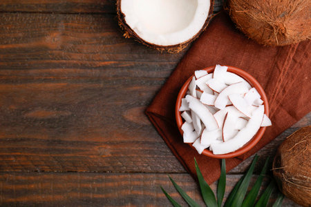 Coconut pieces in bowl, nuts and palm leaf on wooden table, top view. Space for textの写真素材
