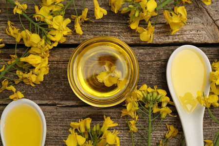 Rapeseed oil in bowl, gravy boats and beautiful yellow flowers on wooden table, flat layの写真素材