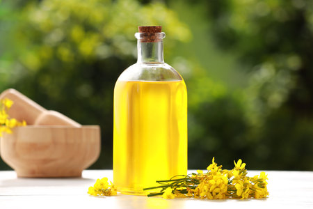 Rapeseed oil in glass bottle and yellow flowers on white wooden table outdoorsの写真素材