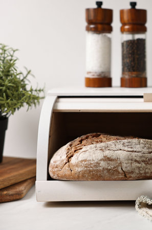 Wooden bread basket with freshly baked loaves on white marble table in kitchenの写真素材