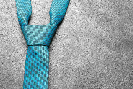One blue necktie on gray textured background, top view. Space for text