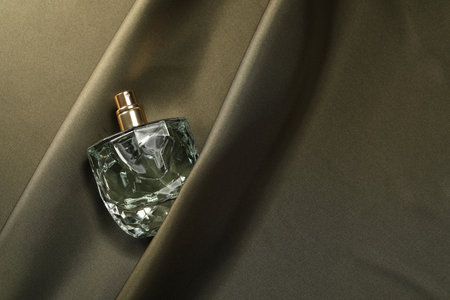 Luxury perfume in bottle on dark silk fabric, top view
