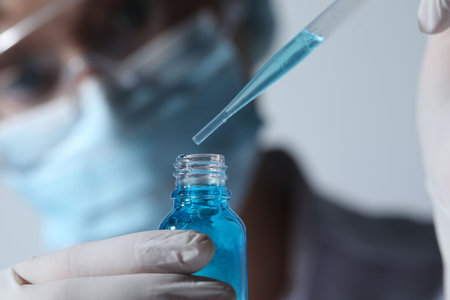 Scientist dripping liquid from pipette into glass bottle on light background, closeupの写真素材