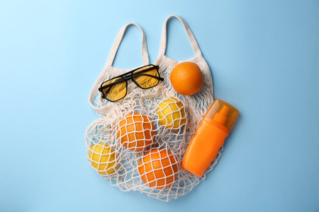 String bag with sunglasses, fruits and sunscreen on light blue background, flat layの写真素材
