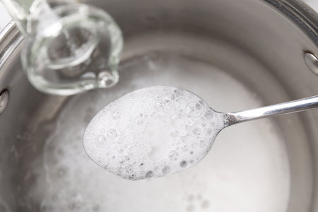 Pouring vinegar into spoon with baking soda over saucepan, closeupの写真素材