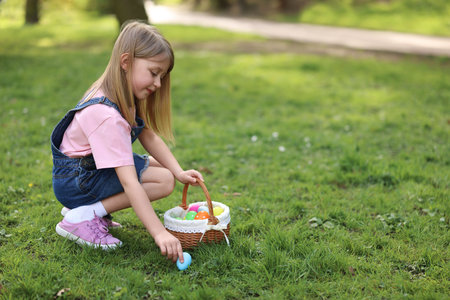 Easter celebration. Cute little girl with bunny ears hunting eggs outdoors, space for text