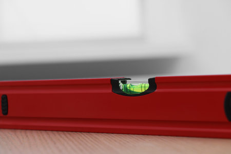 Red building level on wooden table indoors, closeup