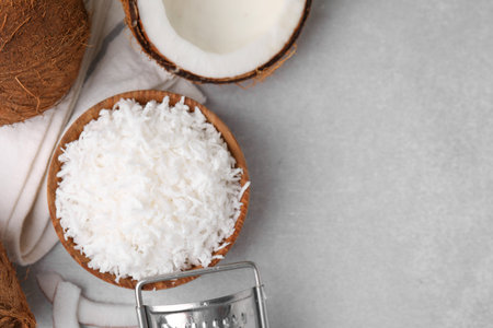 Coconut flakes in bowl, nuts and grater on light gray table, top view. Space for text