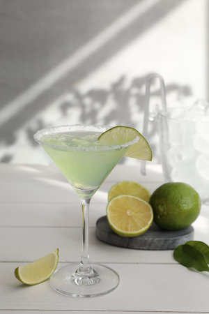Delicious Margarita cocktail in glass and limes on white wooden tableの写真素材