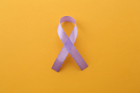 Violet awareness ribbon on orange background, top view