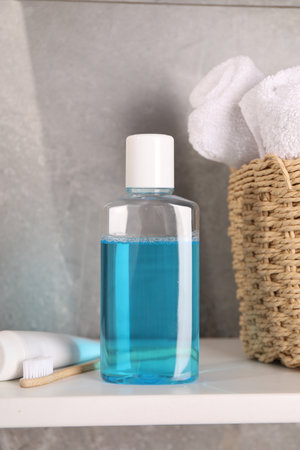 Bottle of mouthwash, toothpaste, toothbrush and towels on shelf in bathroomの写真素材