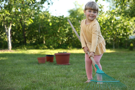 Cute little girl with rake in garden on spring dayの写真素材