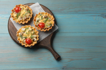 Tasty tartlets with cheese, tomatoes, mushrooms and dill on turquoise wooden table, top view. Space for textの写真素材