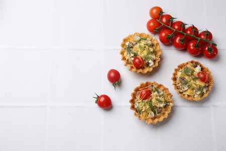 Tasty tartlets with cheese, tomatoes, mushrooms and dill on white tiled table, flat lay. Space for...