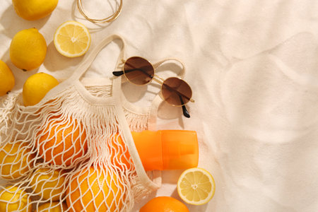 String bag with sunglasses, fruits and sunscreen on sand, flat lay. Space for textの写真素材
