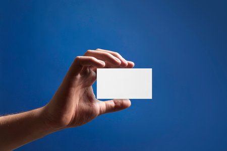 Man with blank business card on blue background, closeup. Mockup for designの写真素材
