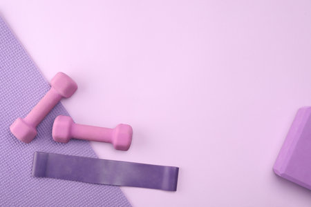 Two dumbbells, yoga block, mat and fitness elastic band on violet background, flat lay. Space for textの写真素材