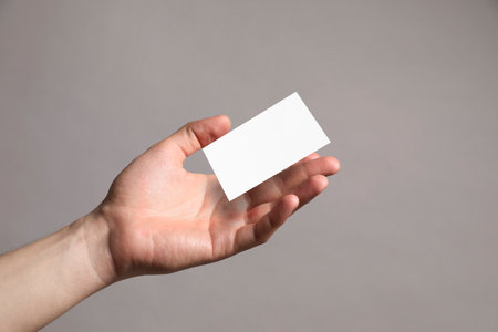 Man with blank business card on gray background, closeup. Mockup for designの写真素材
