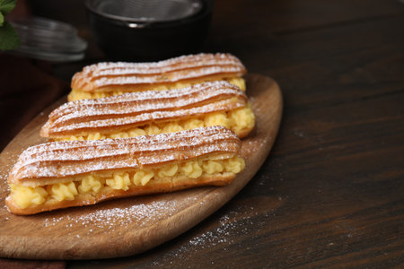 Delicious eclairs filled with cream on wooden table, space for text