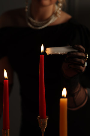 Woman with elegant jewelry lightning up candle indoors, closeupの写真素材