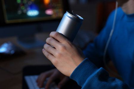 Young man with energy drink playing video game at wooden desk indoors, closeup