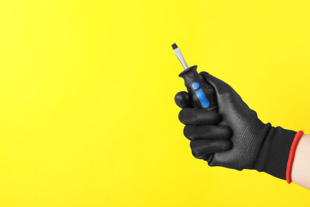 Woman holding small screwdriver on yellow background, closeup. Space for textの写真素材