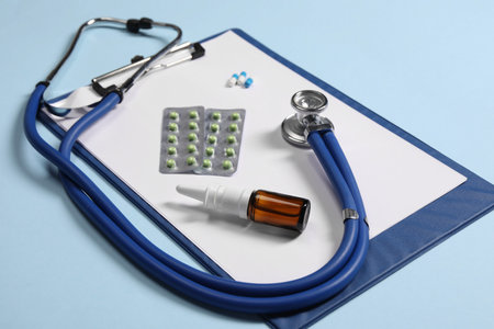 Stethoscope, pills, nasal spray and clipboard on light blue background, closeup. medical toolの写真素材