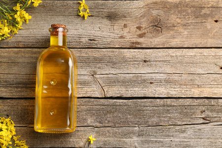 Rapeseed oil in glass bottle and beautiful yellow flowers on wooden table, flat lay. Space for textの写真素材