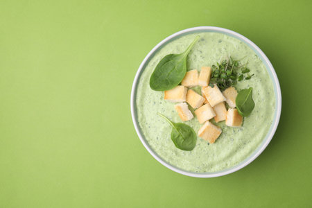 Delicious spinach cream soup with croutons in bowl on green background, top view. Space for textの写真素材