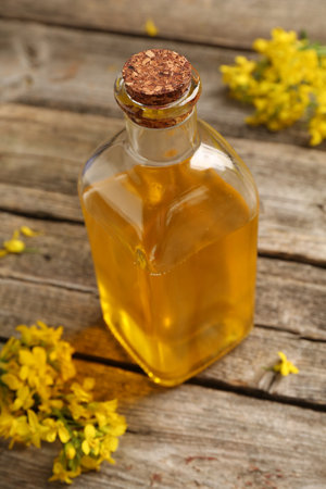 Rapeseed oil in glass bottle and beautiful yellow flowers on wooden table, closeupの写真素材
