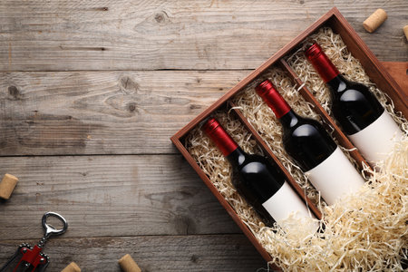 Box with wine bottles, corkscrew and corks on wooden table, flat lay. Space for textの写真素材