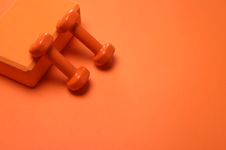 Dumbbells and yoga block on orange background. Space for textの写真素材