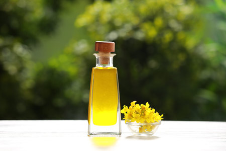 Rapeseed oil in glass bottle and yellow flowers on white wooden table outdoorsの写真素材