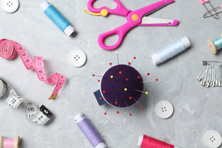Blue pincushion with pins and other sewing tools on gray table, flat layの写真素材