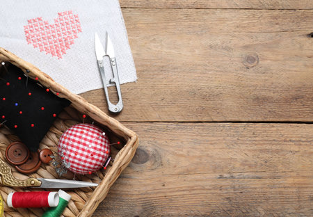 Pincushions with pins and other sewing tools on wooden table, flat lay. Space for textの写真素材
