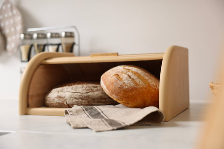 Wooden bread basket with freshly baked loaves on white marble table in kitchenの写真素材