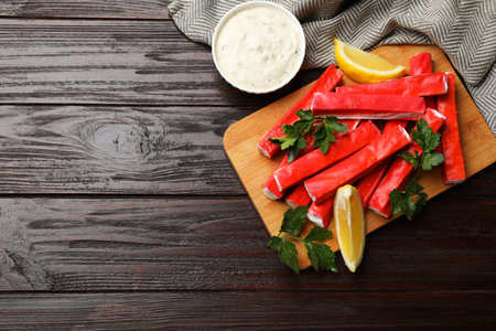 Tasty crab sticks, sauce, parsley and lemon wedges on wooden table, flat lay. Space for textの写真素材
