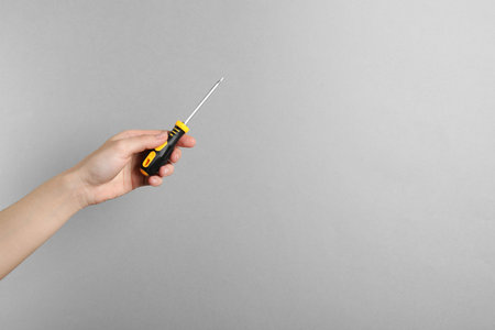 Woman holding screwdriver on gray background, closeup. Space for text