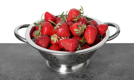 Metal colander with fresh strawberries on gray table against white backgroundの写真素材