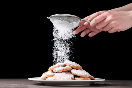 Woman with sieve sprinkling powdered sugar onto cookies at gray table, closeupの写真素材