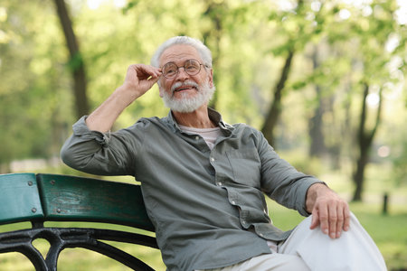 Portrait of happy grandpa with glasses on bench in parkの写真素材