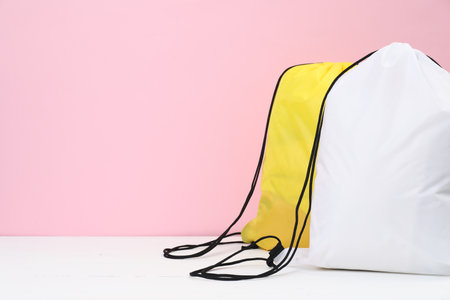 Two drawstring bags on white wooden table against pink background. Space for textの写真素材