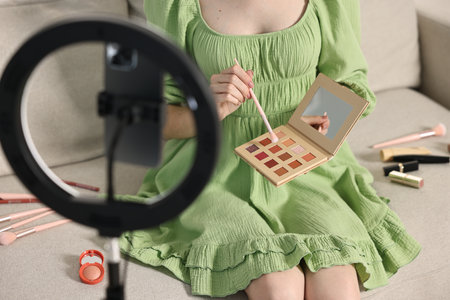 Beauty blogger reviewing eyeshadows and recording video with smartphone and ring lamp at home, closeupの写真素材