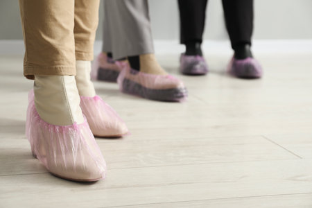 Women wearing pink shoe covers onto different footwear indoors, selective focusの写真素材