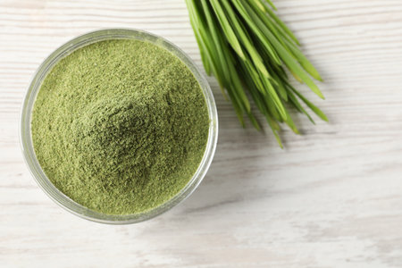 Wheat grass powder in bowl and fresh sprouts on white wooden table, flat lay. Space for textの写真素材