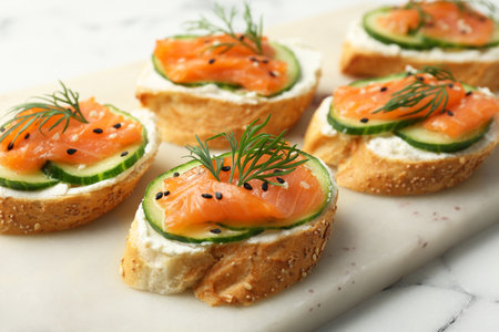 Tasty canapes with salmon, cucumber and cream cheese on white marble table, closeupの写真素材