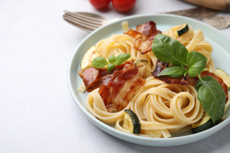 Tasty pasta with bacon and basil on light gray table, space for textの写真素材