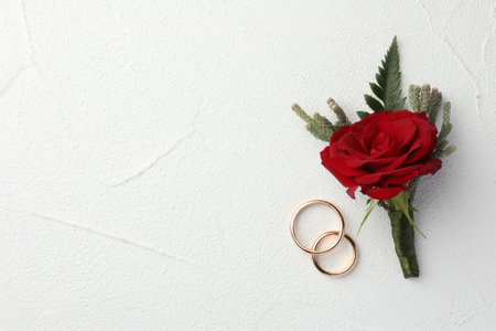 Stylish red boutonniere and rings on white textured table, top view. Space for textの写真素材
